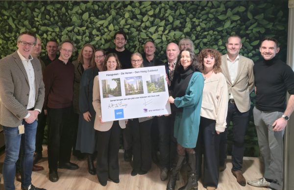 Personen van Wijkontwikkelingsmaatschappij Den Haag Zuidwest met personen van ERA Contour. De personen in het midden houden een ondertekenbord waarop Hoogveen te zien is vast.